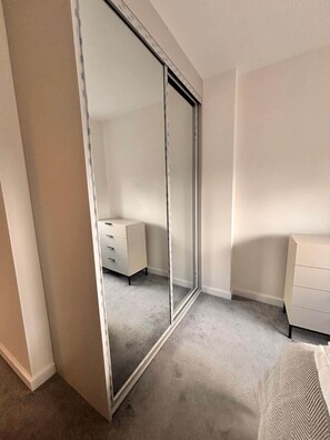 Ein Schlafzimmer mit Schiebetürschrank, weißem Schminktisch und einem Bett mit gemustertem Überwurf.