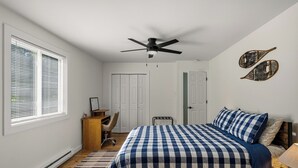 Un dormitorio con cama, escritorio, silla, ventilador de techo y ventana con persianas.