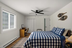 Ein Schlafzimmer mit Bett, Schreibtisch, Stuhl, Deckenventilator und einem Fenster mit Jalousien.