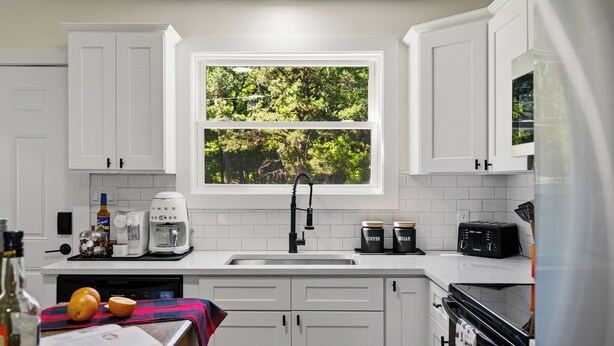 Una cocina moderna con gabinetes blancos, un ventanal con vistas a zonas verdes, una cafetera, un tostador y un refrigerador.