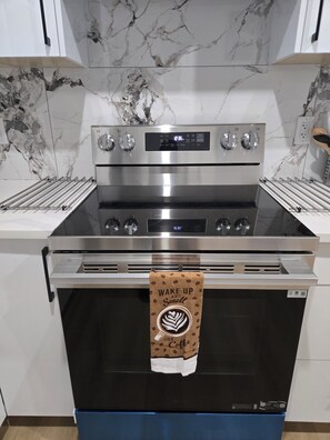 A stainless steel oven with a digital display, a coffee-themed towel hanging from the door, and marble-patterned walls. - Imperial Lodge:3BD Peaceful Getaway Suite+King Bed (Edmonton)