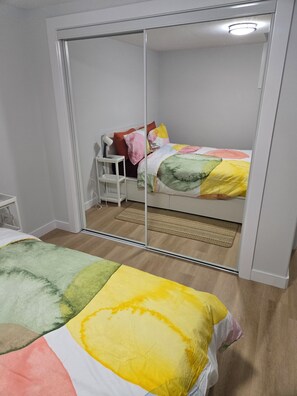 A bedroom with a bed, a bedside table, a mirror, and a wardrobe. - Imperial Lodge:3BD Peaceful Getaway Suite+King Bed (Edmonton)