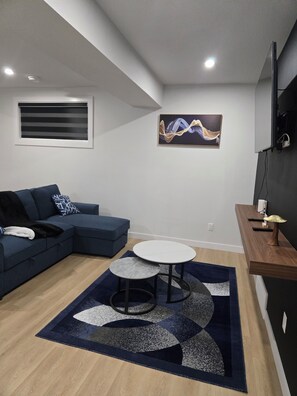 A modern living room with a sectional sofa, a round coffee table, and a painting on the wall. - Imperial Lodge:3BD Peaceful Getaway Suite+King Bed (Edmonton)