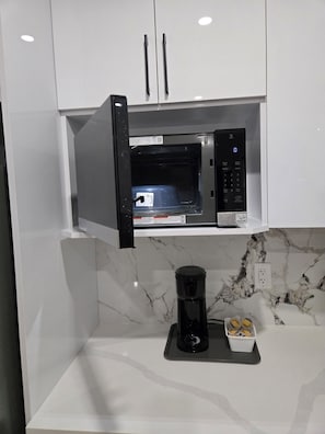 Eine Küche mit integriertem Mikrowellenherd, einer Kaffeemaschine und einem kleinen Behälter auf der Arbeitsfläche.