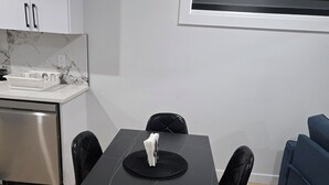 A modern kitchen with white cabinets and a marble backsplash, a dining table with black chairs, and a blue sofa in the living area. - Imperial Lodge:3BD Peaceful Getaway Suite+King Bed (Edmonton)