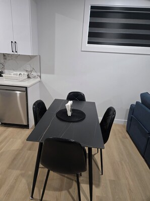 A modern kitchen with white cabinets and a marble backsplash, a dining table with black chairs, and a blue sofa in the living area. - Imperial Lodge:3BD Peaceful Getaway Suite+King Bed (Edmonton)