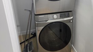 A stacked washer and dryer unit with a control panel, a mop, and a power cord. - Imperial Lodge:3BD Peaceful Getaway Suite+King Bed (Edmonton)