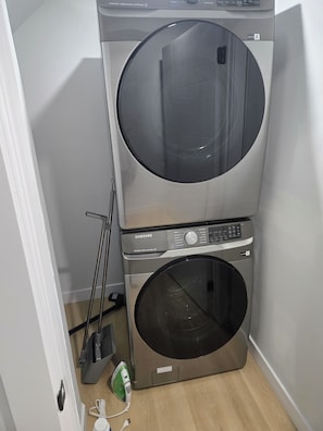 A stacked washer and dryer unit with a control panel, a mop, and a power cord. - Imperial Lodge:3BD Peaceful Getaway Suite+King Bed (Edmonton)