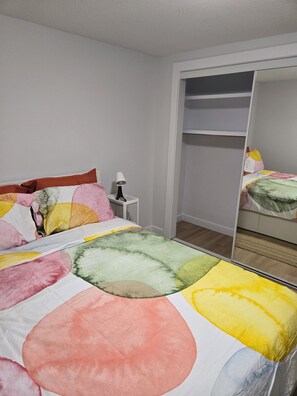 A bedroom with a bed, a bedside table, a lamp, and a wardrobe. - Imperial Lodge:3BD Peaceful Getaway Suite+King Bed (Edmonton)