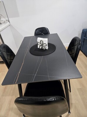 A rectangular dining table with a black marble-like surface, surrounded by four black upholstered chairs. - Imperial Lodge:3BD Peaceful Getaway Suite+King Bed (Edmonton)