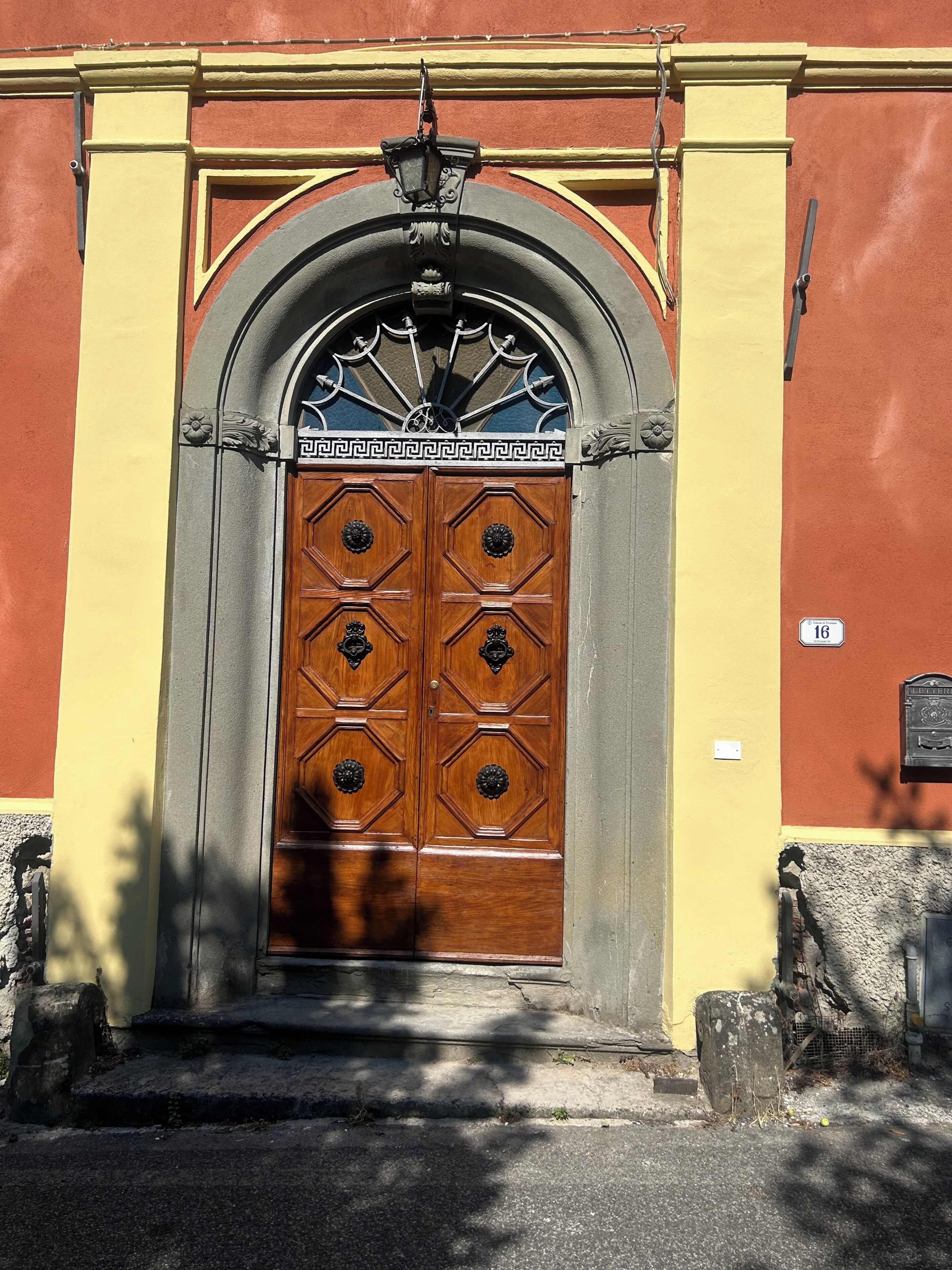 Eine doppelte Holztür mit einem dekorativen Metallbogen darüber, in eine Fassade mit gelber und roter Gestaltung eingelassen.