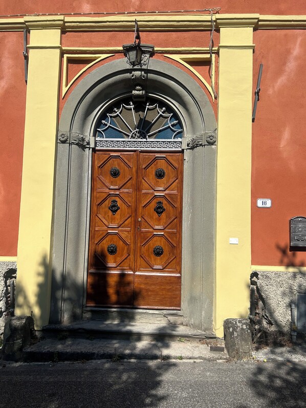 A double wooden door with a decorative metal arch above it, set in a building with a yellow and red facade.