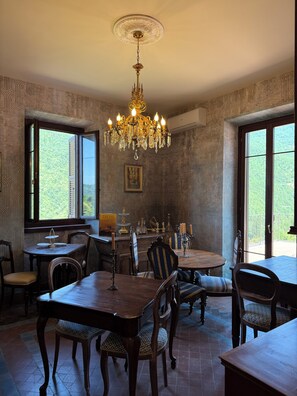 A dining area with a chandelier, patterned wallpaper, and large windows.