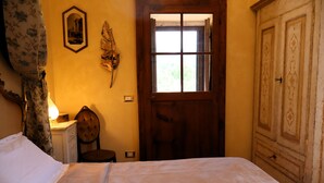 A room with a bed, a wooden door, a chair, a desk with a lamp, and a wall-mounted picture. - Palazzo degli Angeli Palace of Angels (Fivizzano)