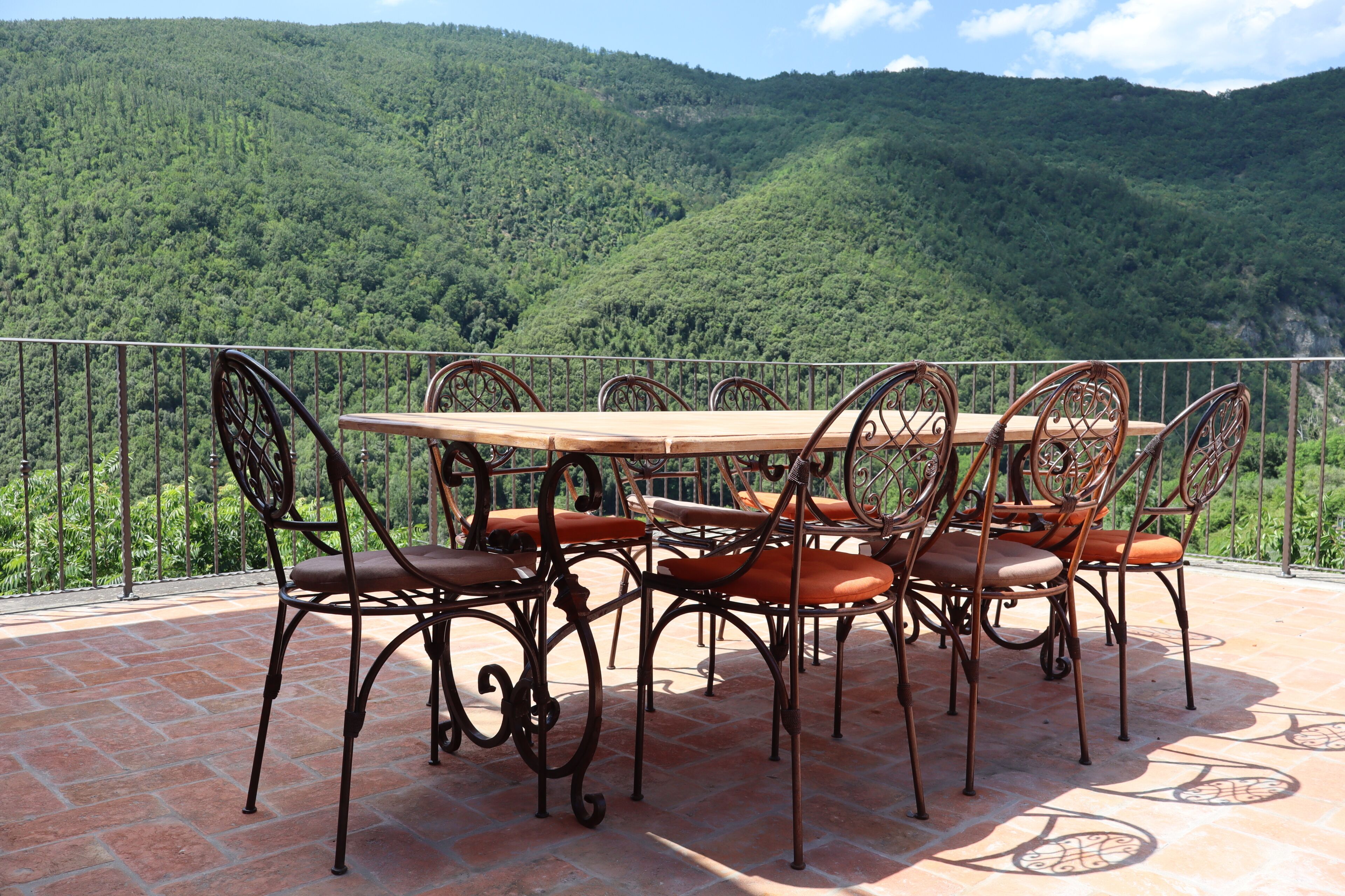 A terrace with a table and chairs, overlooking a forested hillside.