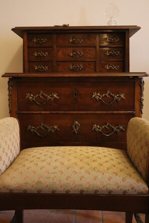 A wooden chest of drawers with ornate handles and a floral-patterned upholstered chair in front.