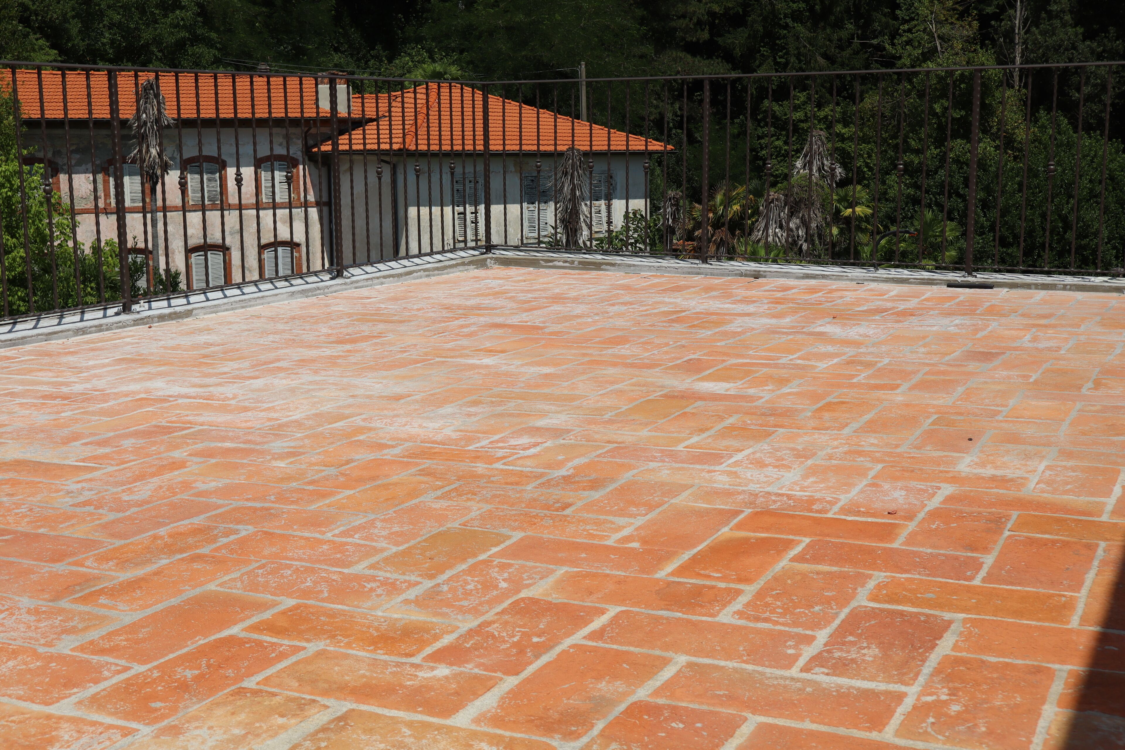 Un cortile con piastrelle in terracotta, una recinzione in metallo e un edificio con tetto in tegole.