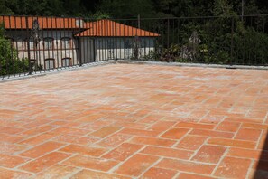 Um pátio com telhas de terracota, uma cerca de metal e um edifício com telhado telhado.