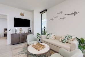 A modern living room with a sofa, armchairs, a coffee table, a flat-screen TV, a wall clock, and decorative wall decals. - Luxury 4-bedroom condo At 72 Park With Gym, Pool, Tiki bar and Beach Service (Miami Beach)