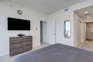 A modern bedroom with a large bed, a flat-screen TV mounted on the wall, a built-in bench with storage, a large mirror, and a door leading to a balcony. - Luxury 4-bedroom condo At 72 Park With Gym, Pool, Tiki bar and Beach Service (Miami Beach)