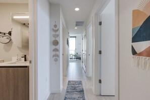 Un couloir avec un tapis bleu, des murs blancs et une porte ornée d’une œuvre d’art géométrique.