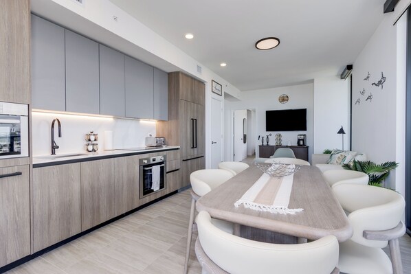 A modern kitchen with a central island, built-in appliances, and a dining area with a long table and chairs.