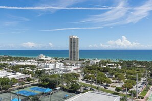 A high-rise building with a view of the ocean and a tennis court in the foreground. - Luxury 4-bedroom condo At 72 Park With Gym, Pool, Tiki bar and Beach Service (Miami Beach)