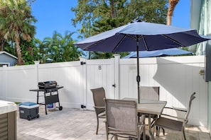 Eine Terrasse im Freien mit Tisch, Stühlen, einem Grill und einem weißen Zaun.