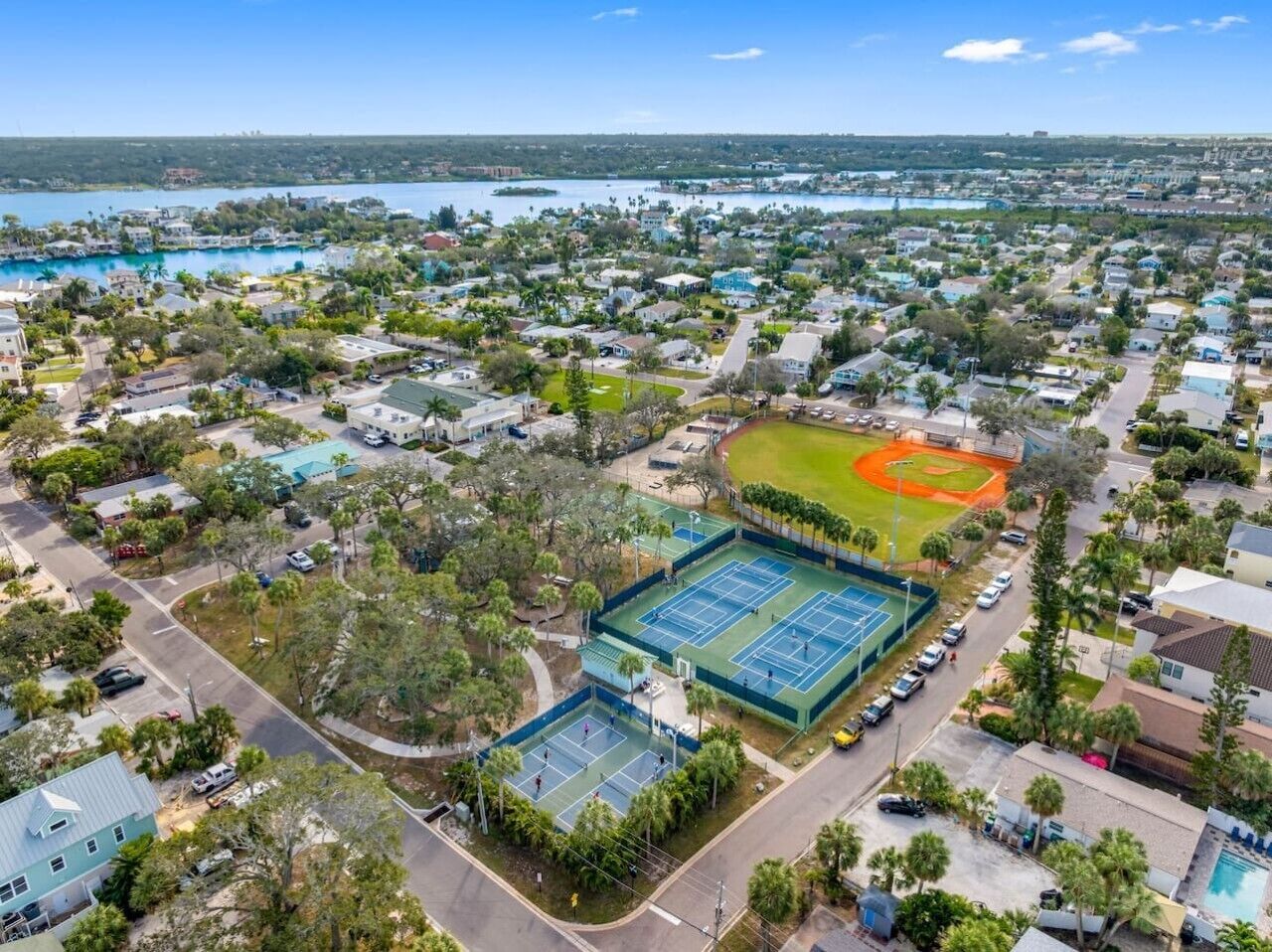 An aerial view of a residential area with houses, a tennis court, and a baseball field.