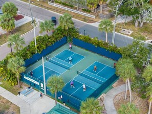 Luftaufnahme eines Tennisplatzes, umgeben von Palmen und einem Bürgersteig.
