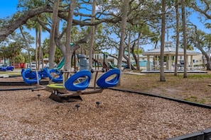 Ein Spielplatz mit einer Wippe, Schaukeln und einer Rutsche.