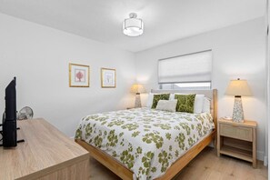 Ein Schlafzimmer mit einem Bett, Nachttischen, einem Schreibtisch und einer Deckenleuchte.