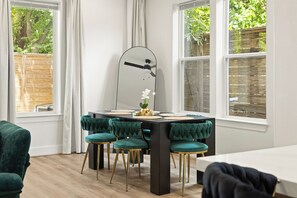 Een eetgedeelte met een zwarte tafel, vier teal-kleurige fauteuils en een moderne vloerlamp.