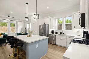 A modern kitchen with a central island, stainless steel appliances, and a dining area with a green sofa and chairs. - The Suite Spot: 4BR with 2 King Suites and Private Patio near NRG Stadium (Houston)