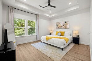 Een slaapkamer met een bed, een plafondventilator, een raam en een schilderij aan de muur.