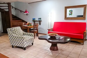 A living room with a red sofa, patterned armchair, dining table, and a coffee table with a bowl. - Garden Paradise, Walk to the Beach (Tamarindo)