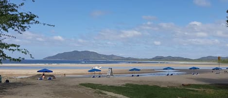 A beach with umbrellas and a boat, a clear sky, and distant mountains.