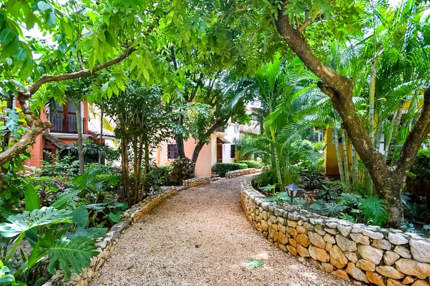 A pathway leading through a lush garden with stone walls and various tropical plants.