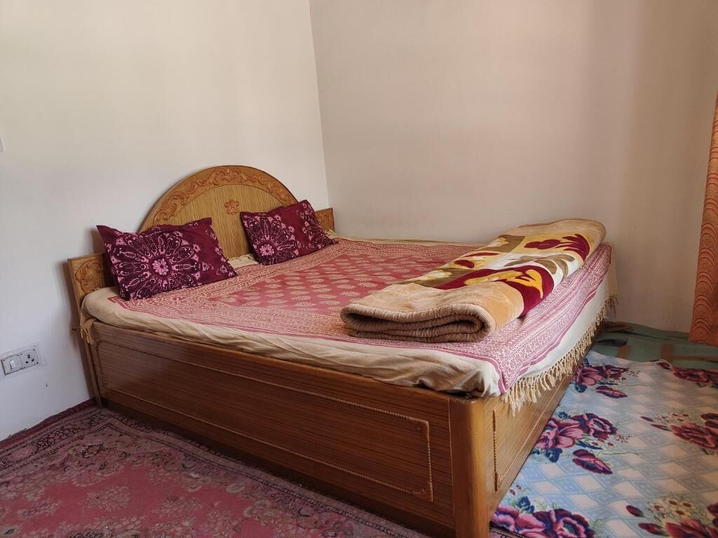Una cama individual con cabecera de madera, dos almohadas, una colcha estampada y una manta doblada.