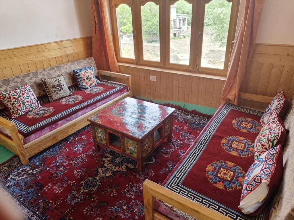Una habitación tradicional con un banco de madera, una mesita pequeña y un tapete estampado.