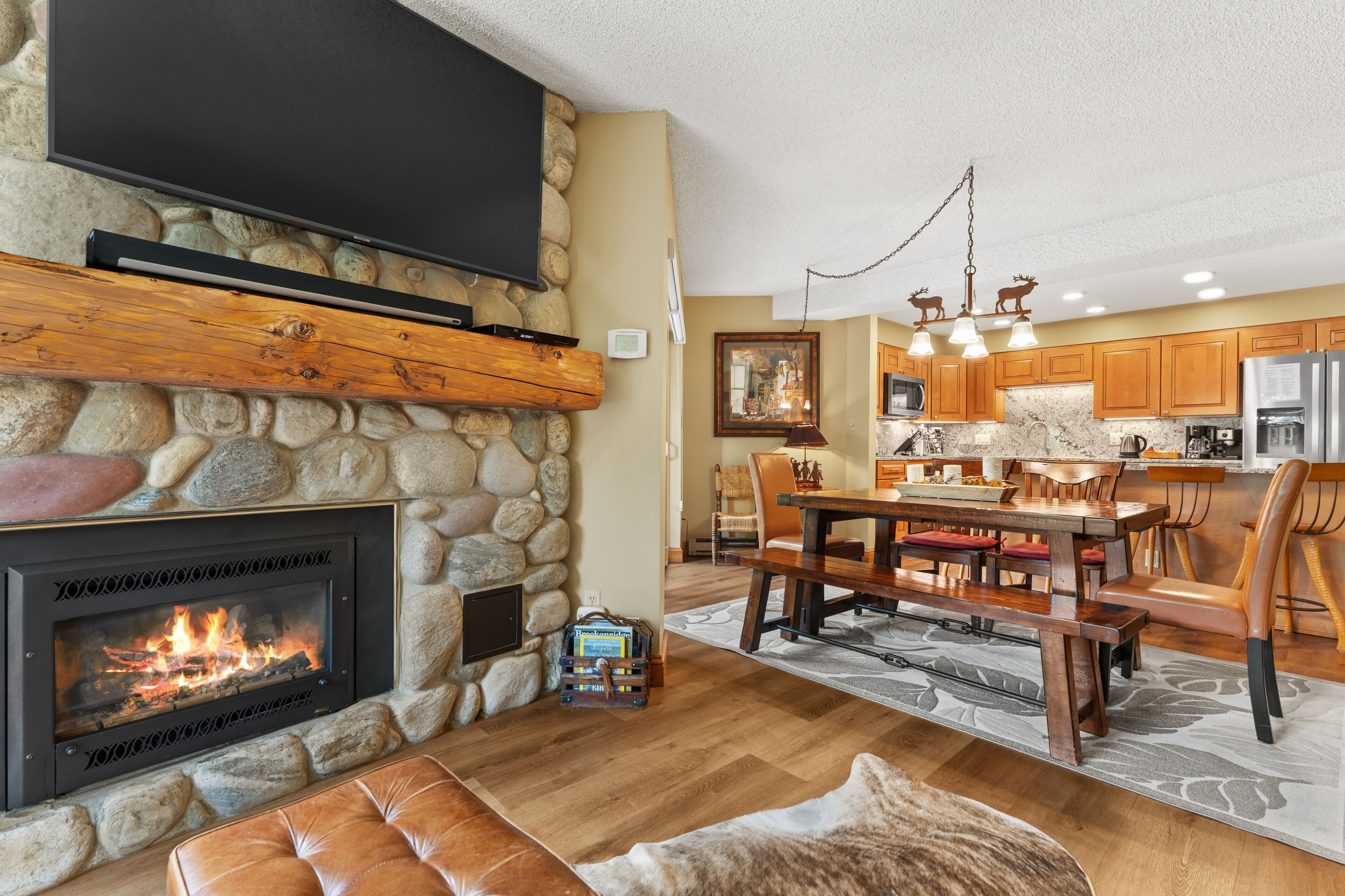 Una sala de estar moderna con chimenea de piedra, televisor de pantalla plana montado encima y un rincón de estar acogedor con un reposapiés de cuero.