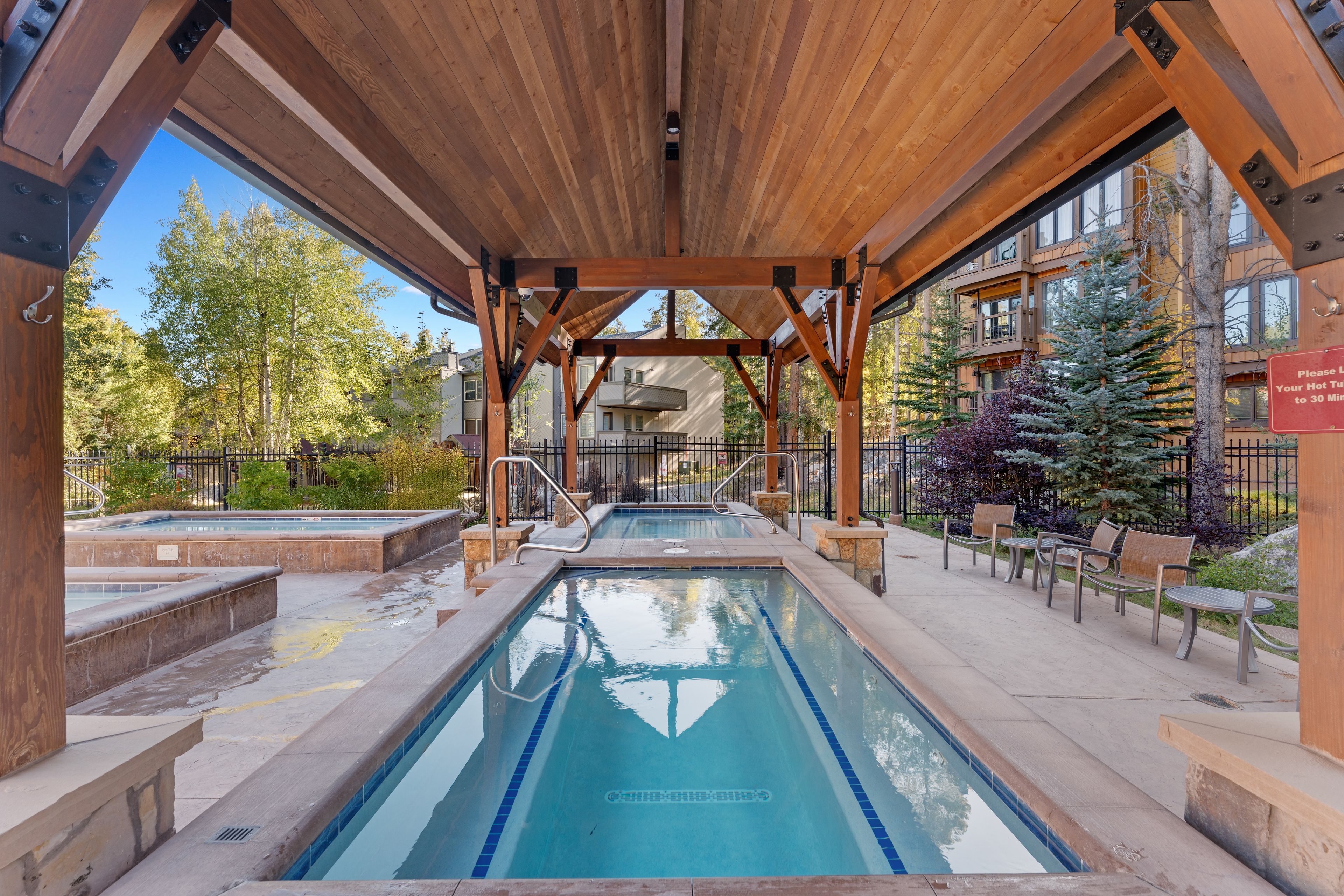 A covered outdoor swimming pool with wooden beams and a clear view of the surrounding buildings and trees.