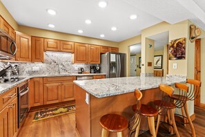 A kitchen with wooden cabinets, granite countertops, stainless steel appliances, and a bar area with stools. - 2BR Breckenridge Retreat | River Views, Pool & Hot Tubs Near Ski Lift (Breckenridge)