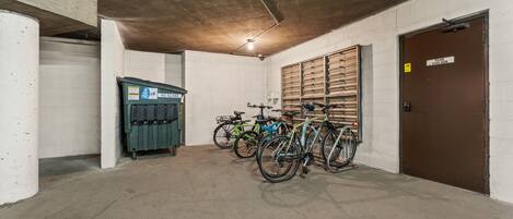 Un parking à vélos avec des bicyclettes appuyées contre le mur, une poubelle et une porte fermée avec une pancarte.