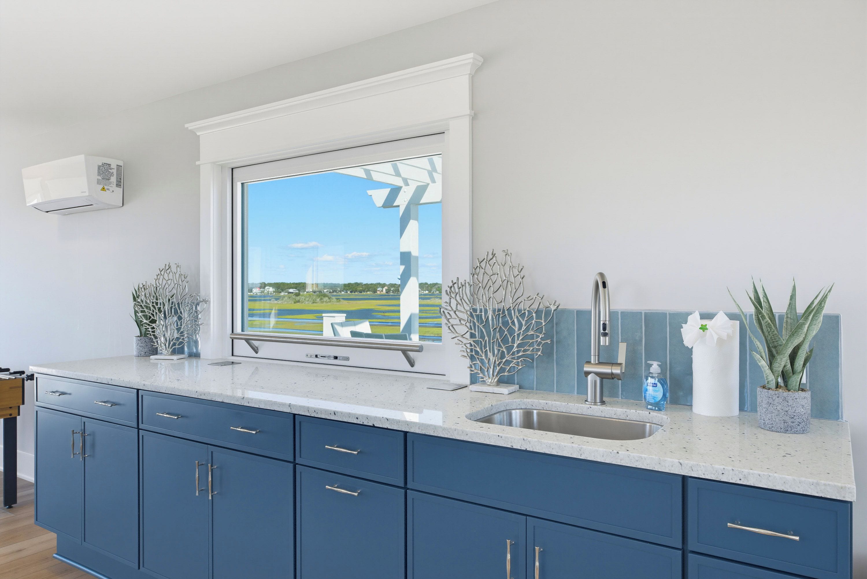 A modern kitchen with a large window, a stainless steel sink, and blue cabinets.