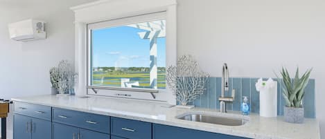 A modern kitchen with a large window, a stainless steel sink, and blue cabinets.