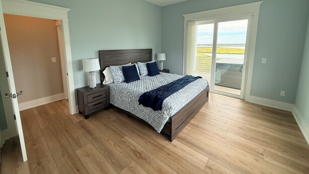 A bedroom with a bed, bedside tables, a ceiling fan, and a view through a sliding glass door. - Soundfront hot tub and rooftop deck (Surf City)