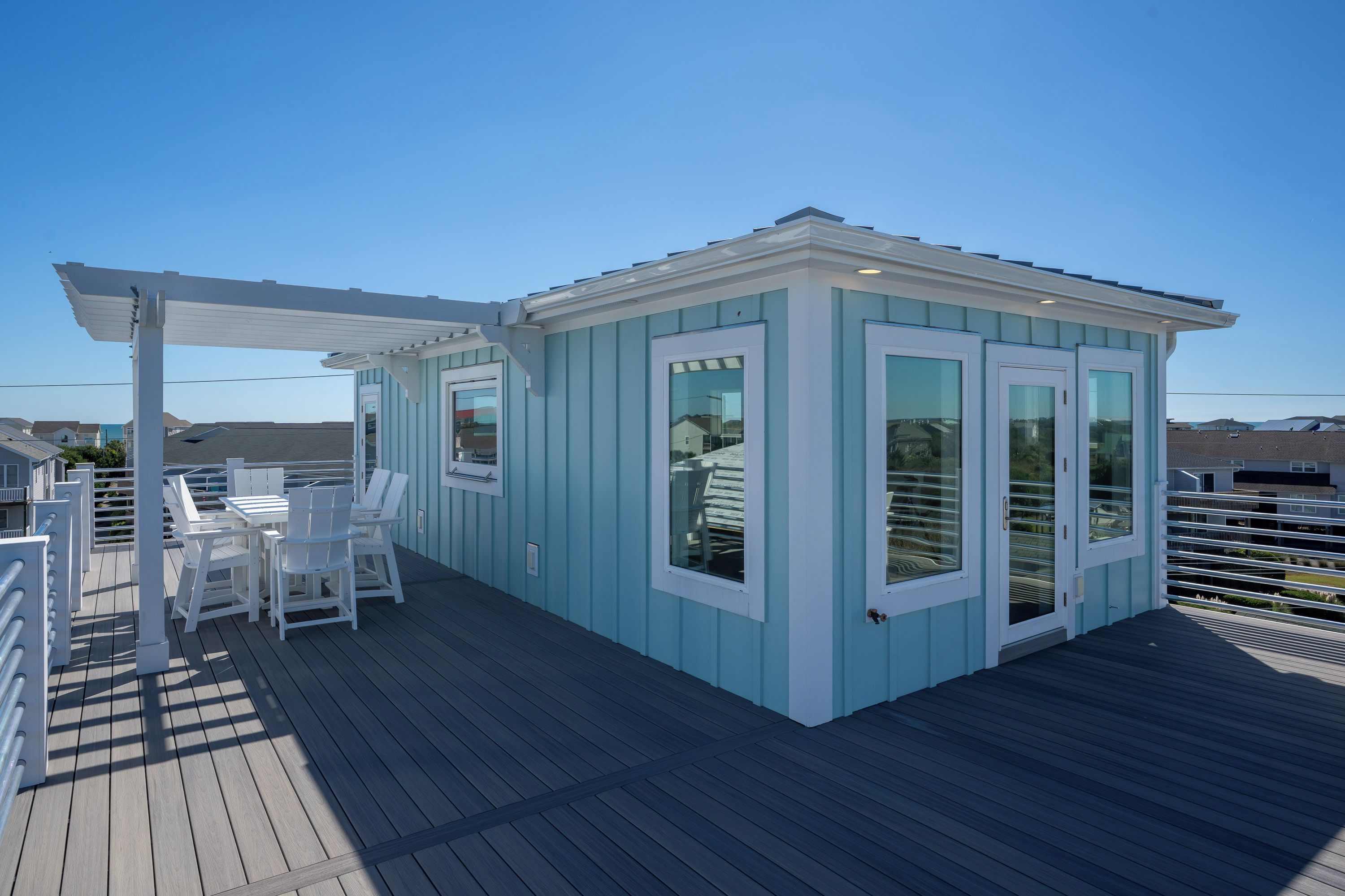A small, light blue building with a covered deck area, white chairs, and a table.