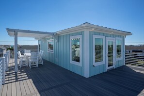 A small, light blue building with a covered deck area, white chairs, and a table. - Soundfront hot tub and rooftop deck (Surf City)