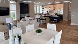 A modern kitchen with a central island, pendant lighting, and a person cooking. - Soundfront hot tub and rooftop deck (Surf City)